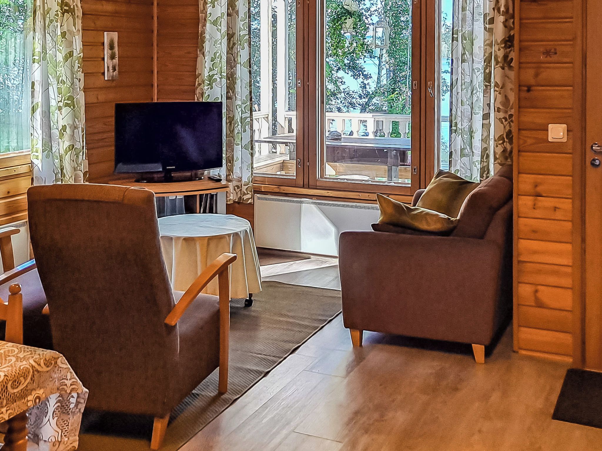 Interior acogedor de una cabaña con televisor, dos sofás, una mesita y ventana con vistas al exterior.