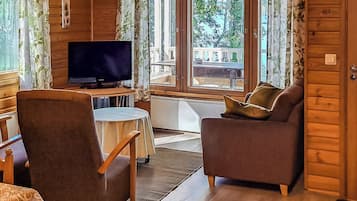 Interior acogedor de una cabaña con televisor, dos sofás, una mesita y ventana con vistas al exterior.