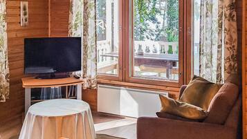 Ein Zimmer mit Fernseher auf einem Schrank, einer Couch, einem kleinen Tisch mit Tischdecke und einem Fenster mit Vorhängen.