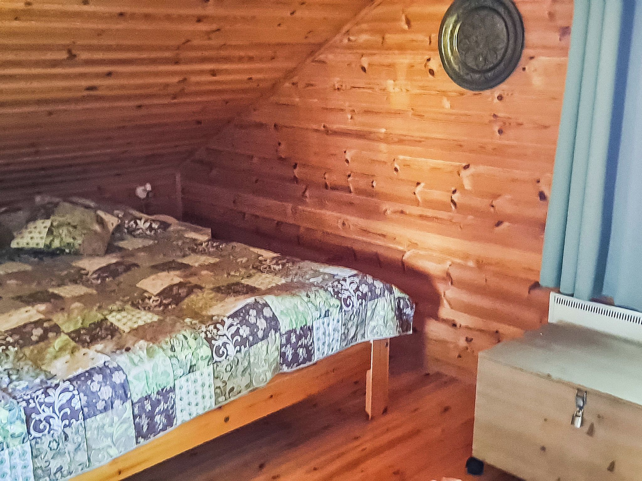 Una habitación de cabaña de madera con una cama, un pequeño aparador de madera y una ventana con cortinas.