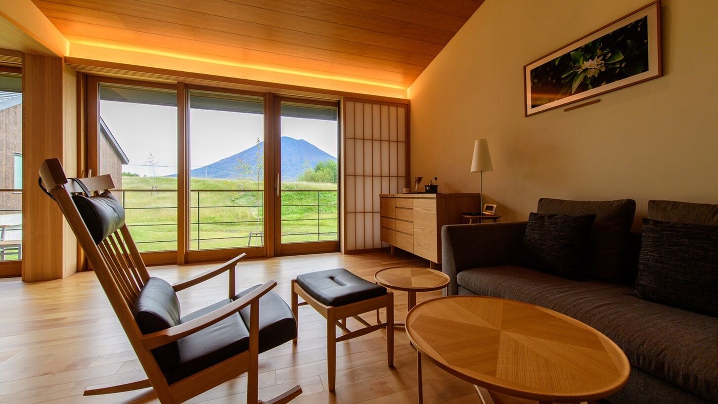 A room with a sofa, a rocking chair, a small table, and a view of a mountain through large sliding doors.