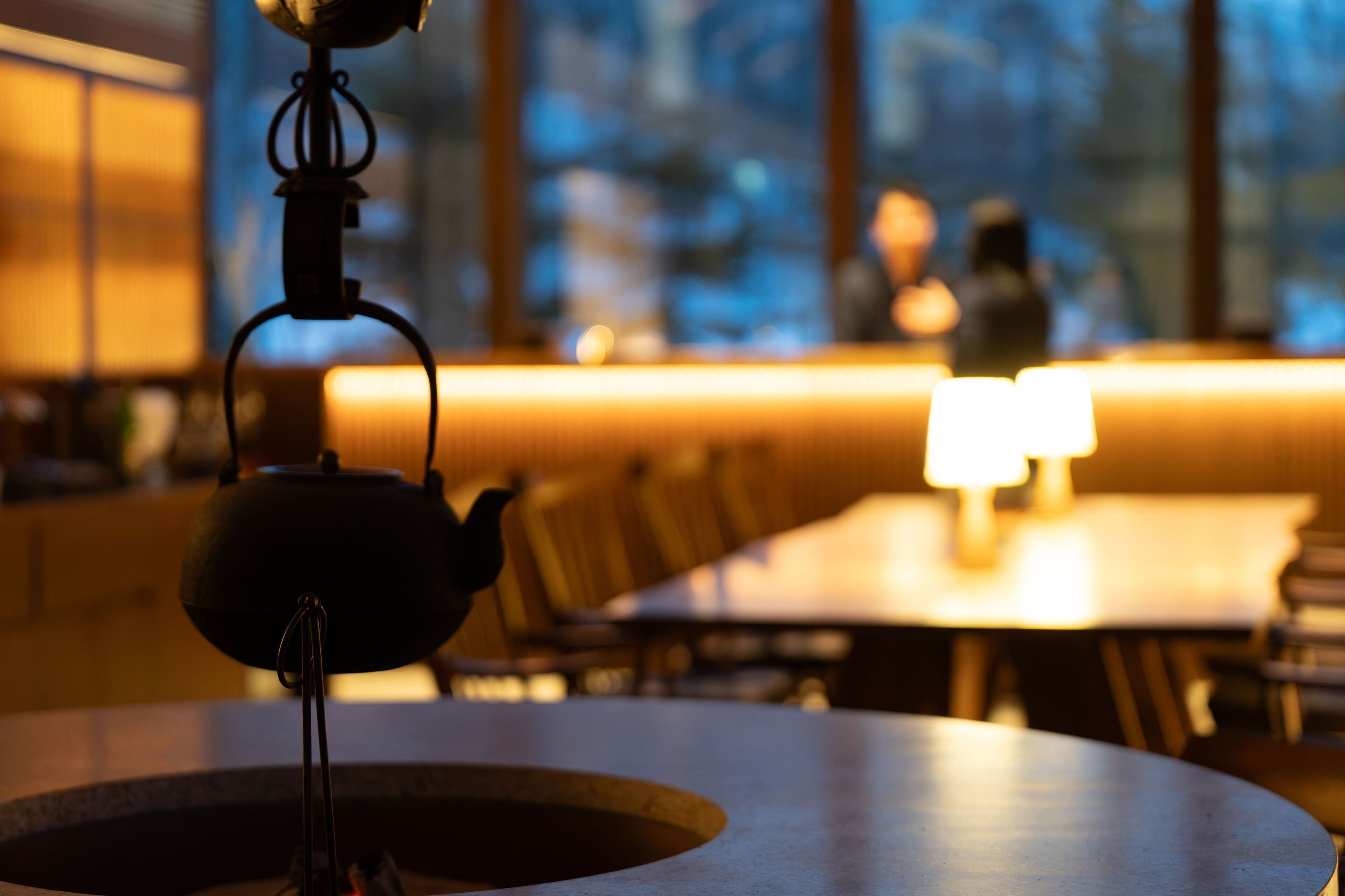 A table with a teapot in the foreground and a blurred background of a restaurant setting.