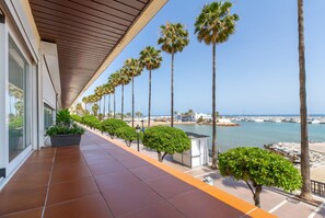 A corridor with a tiled floor, palm trees, and a view of the sea and boats. - Apartment 'En 1ª Línea De Playa' with Sea View, Shared Pool and Wi-Fi (Marbella)