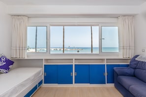 A room with a bed, a sofa, a window with a view of the sea, and blue cabinets.
