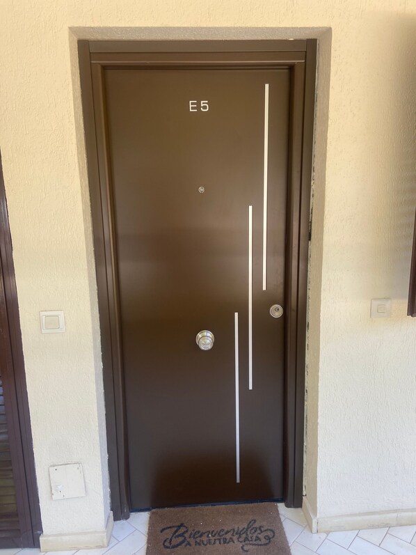 Una puerta marrón con la etiqueta 'E5' y un felpudo que dice 'Bienvenidos'.