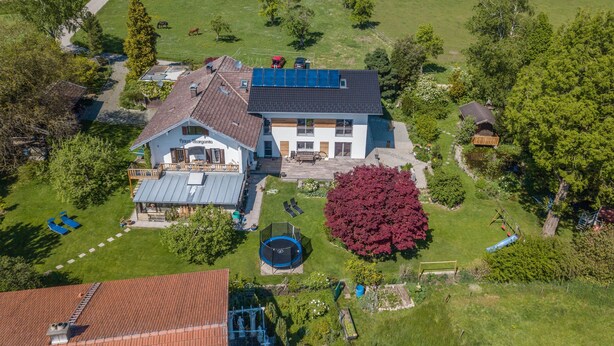 A two-story house with a large front yard, solar panels, and a trampoline. - Apartment "Julia" with Lake View, Mountain View, Wi-Fi, Garden & Terrace (Taching am See)