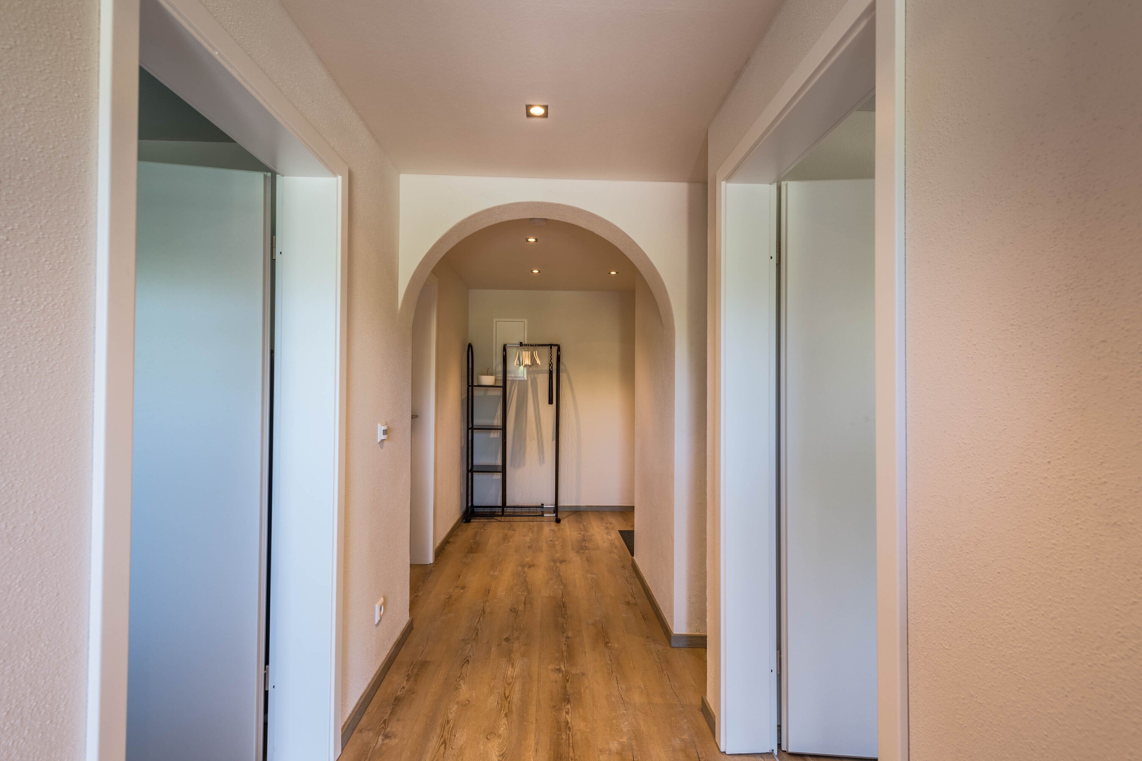 A hallway with a wooden floor, white walls, and an arched ceiling.