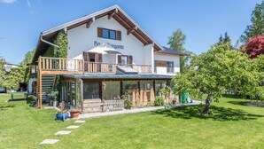 A two-story building with a balcony, a covered front porch, and a well-maintained lawn. - Apartment "Julia" with Lake View, Mountain View, Wi-Fi, Garden & Terrace (Taching am See)