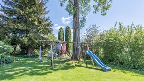 A playground with a slide and swings, surrounded by trees and grass. - Apartment "Julia" with Lake View, Mountain View, Wi-Fi, Garden & Terrace (Taching am See)