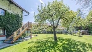 A residential property with a staircase leading to a deck, a tree in the yard, and a house with a sloped roof. - Apartment "Julia" with Lake View, Mountain View, Wi-Fi, Garden & Terrace (Taching am See)