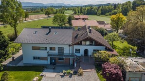 Une maison à deux étages avec un toit en pente, un porche à l’avant et une allée pavée.