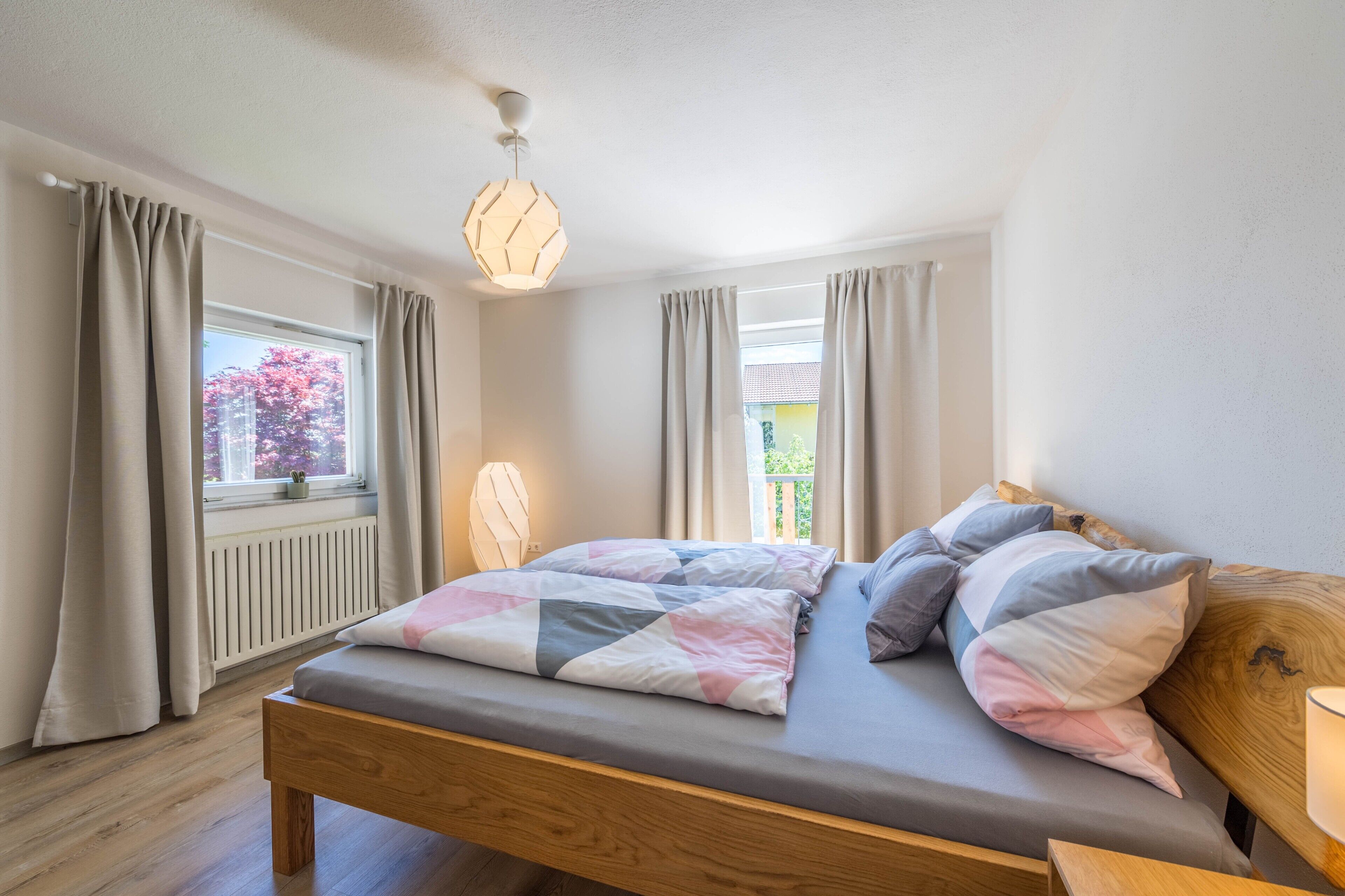 A bedroom with a wooden bed, a window with curtains, a radiator, and a hanging light fixture.