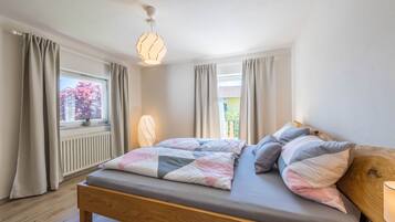 A bedroom with a wooden bed, a window with curtains, a radiator, and a hanging light fixture.