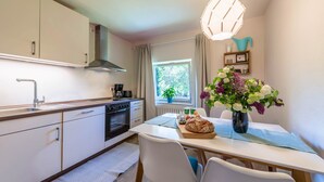 Une cuisine de taille réduite avec une table à manger, des chaises, un vase de fleurs et une fenêtre avec des rideaux.