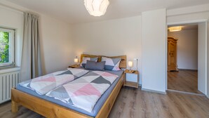 Une chambre à coucher avec un lit en bois, deux tables de chevet, un luminaire suspendu et une vue sur une porte en bois.