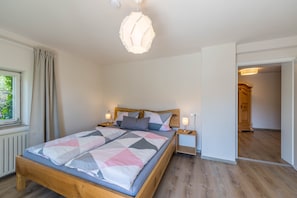 Un dormitorio con una cama de madera, dos mesitas de noche, una lámpara colgante y vistas a una puerta de madera.