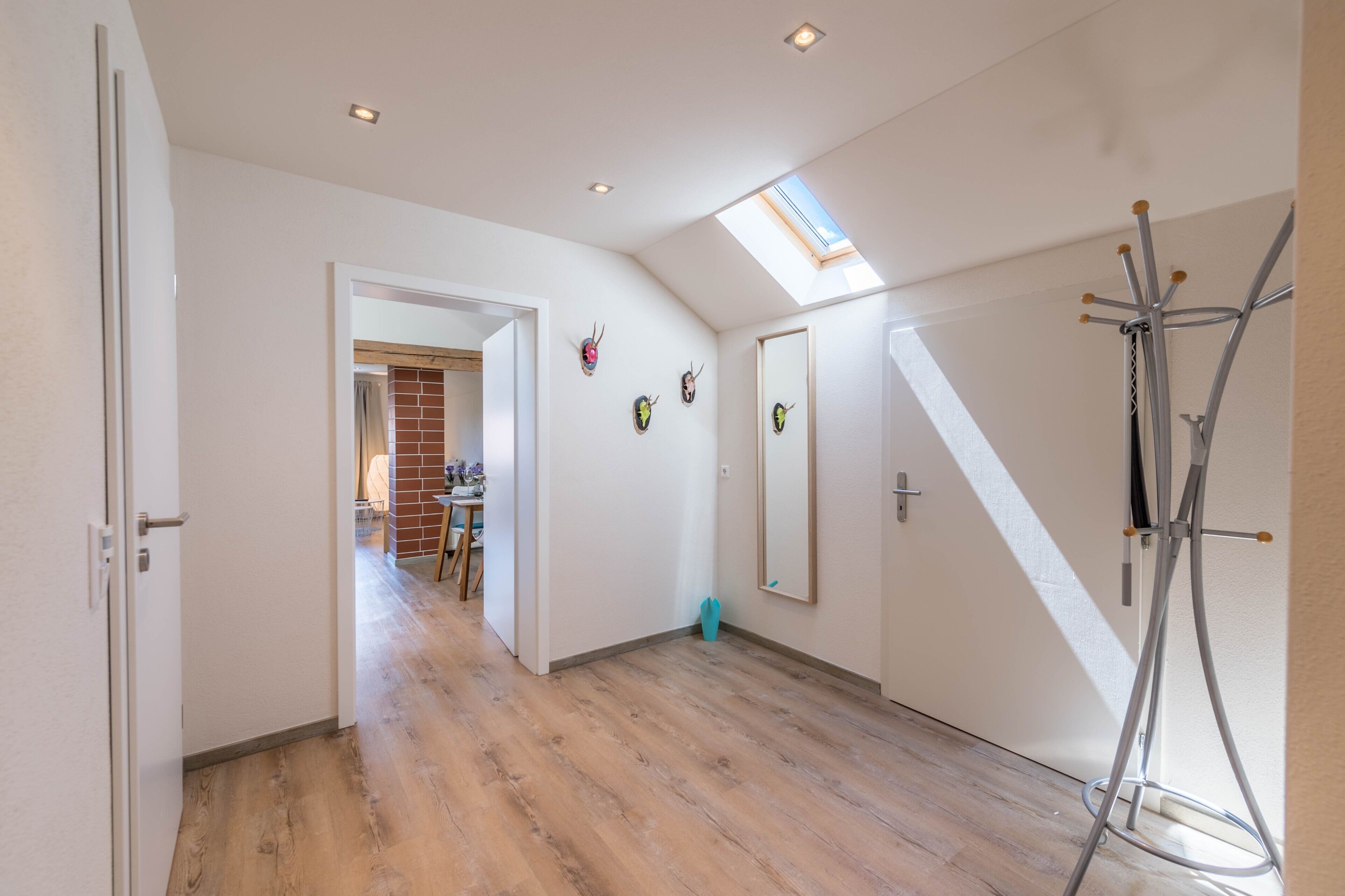 Une pièce avec un plafond en pente, un puits de lumière, un porte-manteau et un miroir au mur.