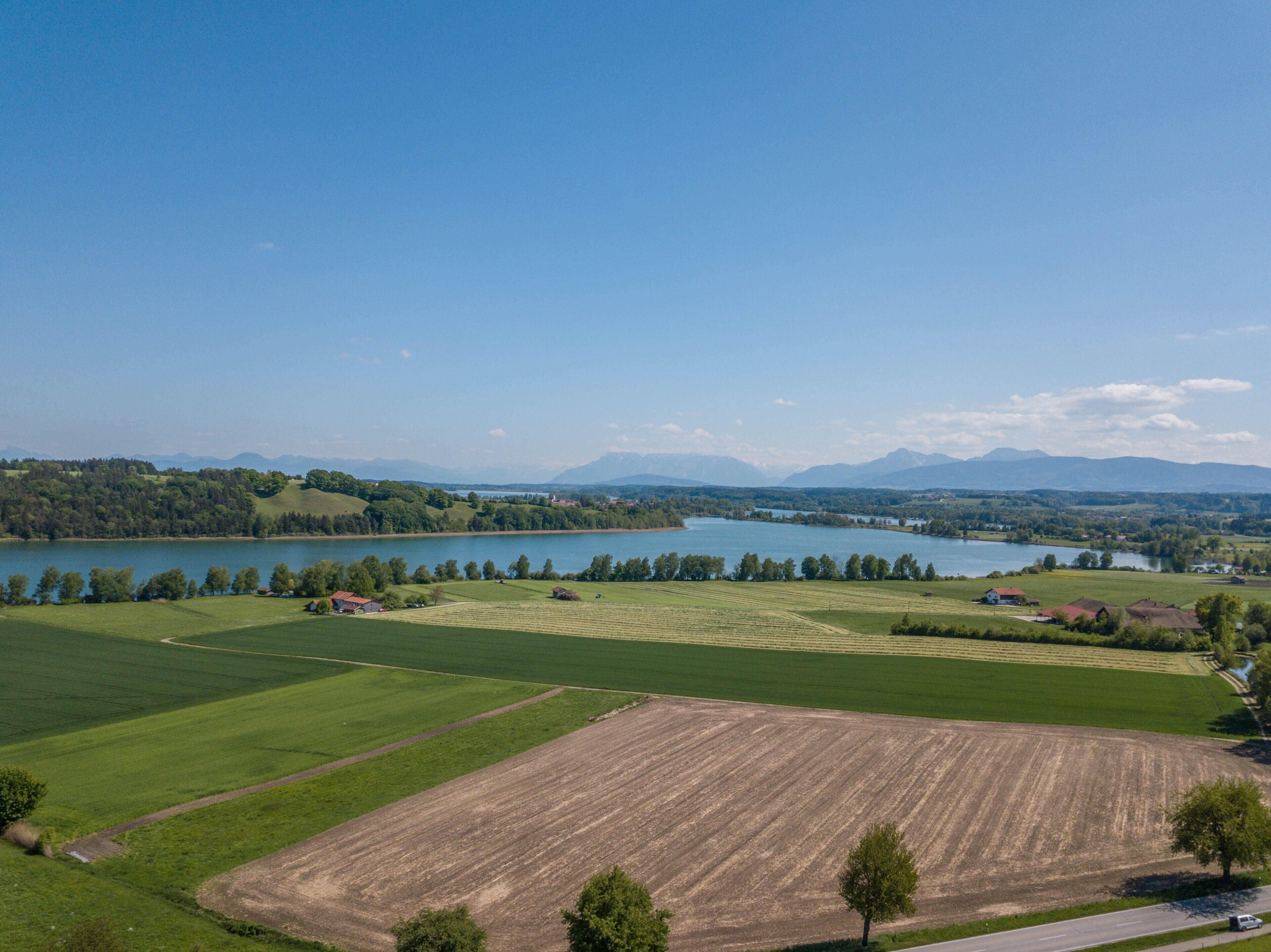 Een landelijk landschap met velden, een meer en verre bergen.