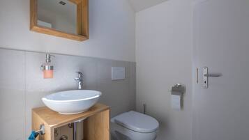 A bathroom with a wooden vanity, white sink, and toilet.