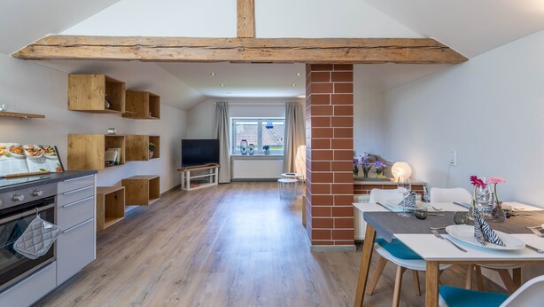 Een moderne keuken met houten balken, een eethoek met een bakstenen zuil, en uitzicht op buiten door een raam.