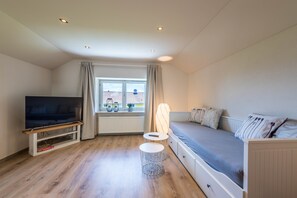 Ein Zimmer mit Fernseher, einer Couch, einem kleinen Tisch und einem Fenster mit Vorhängen.
