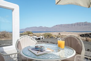 Une table avec un carnet, des lunettes et un verre de jus d’orange, donnant sur un paysage montagneux.