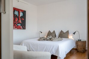Une chambre à coucher comprenant un lit, des oreillers, une lampe de chevet, une table de chevet en bois et une œuvre d’art murale.