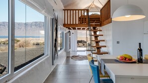 A modern interior with large windows, a wooden staircase, and a dining area with a fruit plate. - Modern House "El Loft" with Sea and Mountain View, Wi-Fi & Terrace (Famara)
