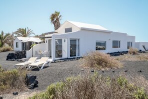 Edifici modern i blanc amb terrat pla, finestres grans i sòl sorrenc amb gandules.
