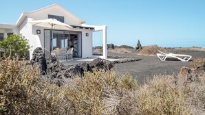 A modern white building with a glass door, a patio with a white umbrella, and a view of the ocean. - Modern House "El Loft" with Sea and Mountain View, Wi-Fi & Terrace (Famara)