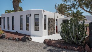 Un edificio moderno blanco con entrada de pared de piedra, un jardín de cactus y cielo despejado.