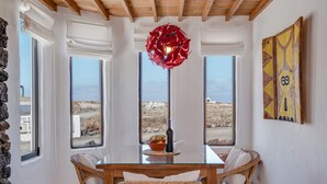 Un comedor con mesa de vidrio, sillas de mimbre, lámpara decorativa roja y vistas del paisaje a través de amplios ventanales.