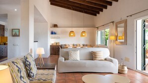 Un amplio salón con un sofá, dos mesas y lámparas colgantes.