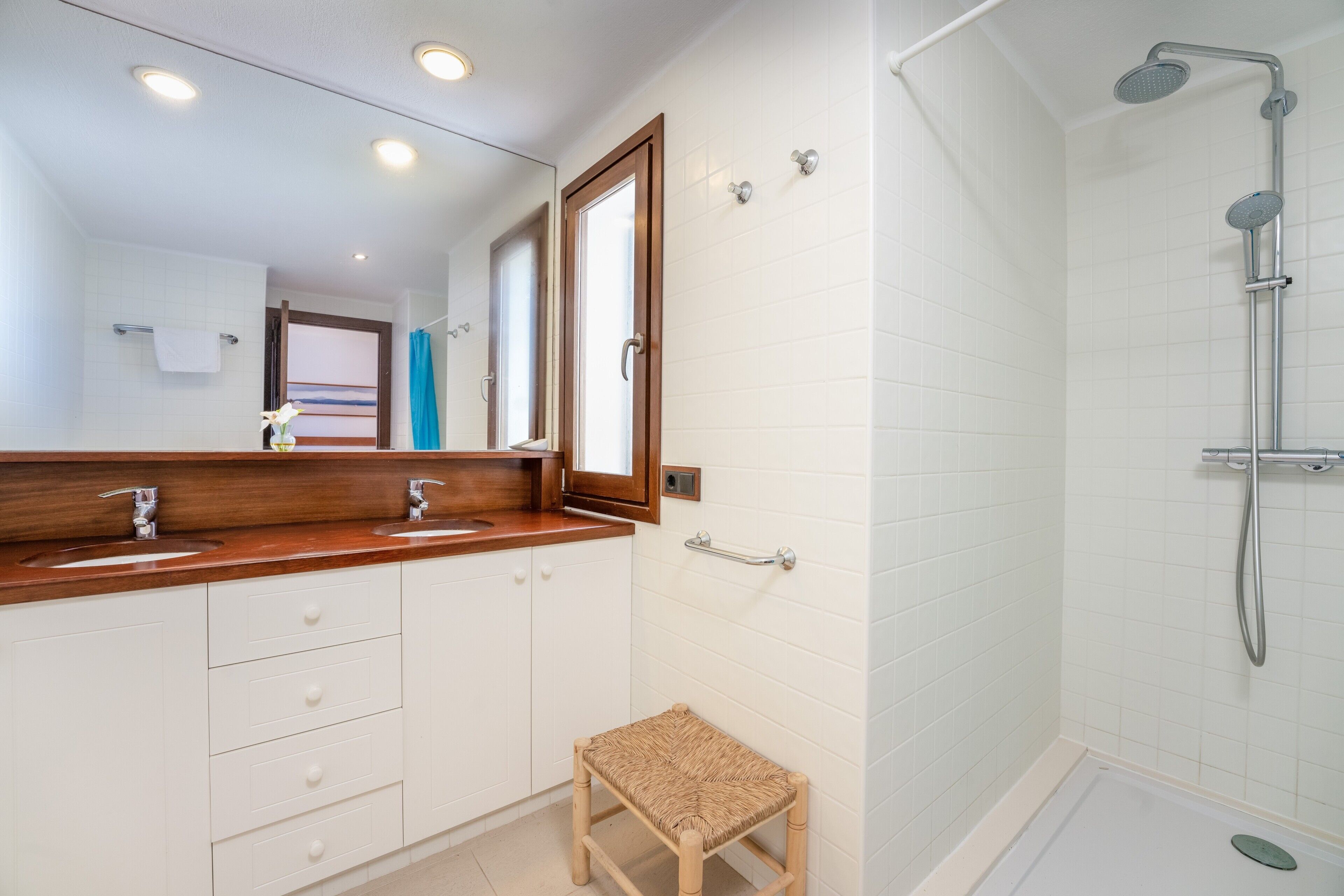 Un baño con tocador de madera, ducha y un pequeño taburete.