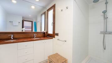 Un baño con tocador de madera, ducha y un pequeño taburete.
