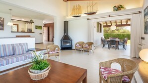 Een ruime woonkamer met een houten tafel, rieten stoelen, een bank en een open haard.
