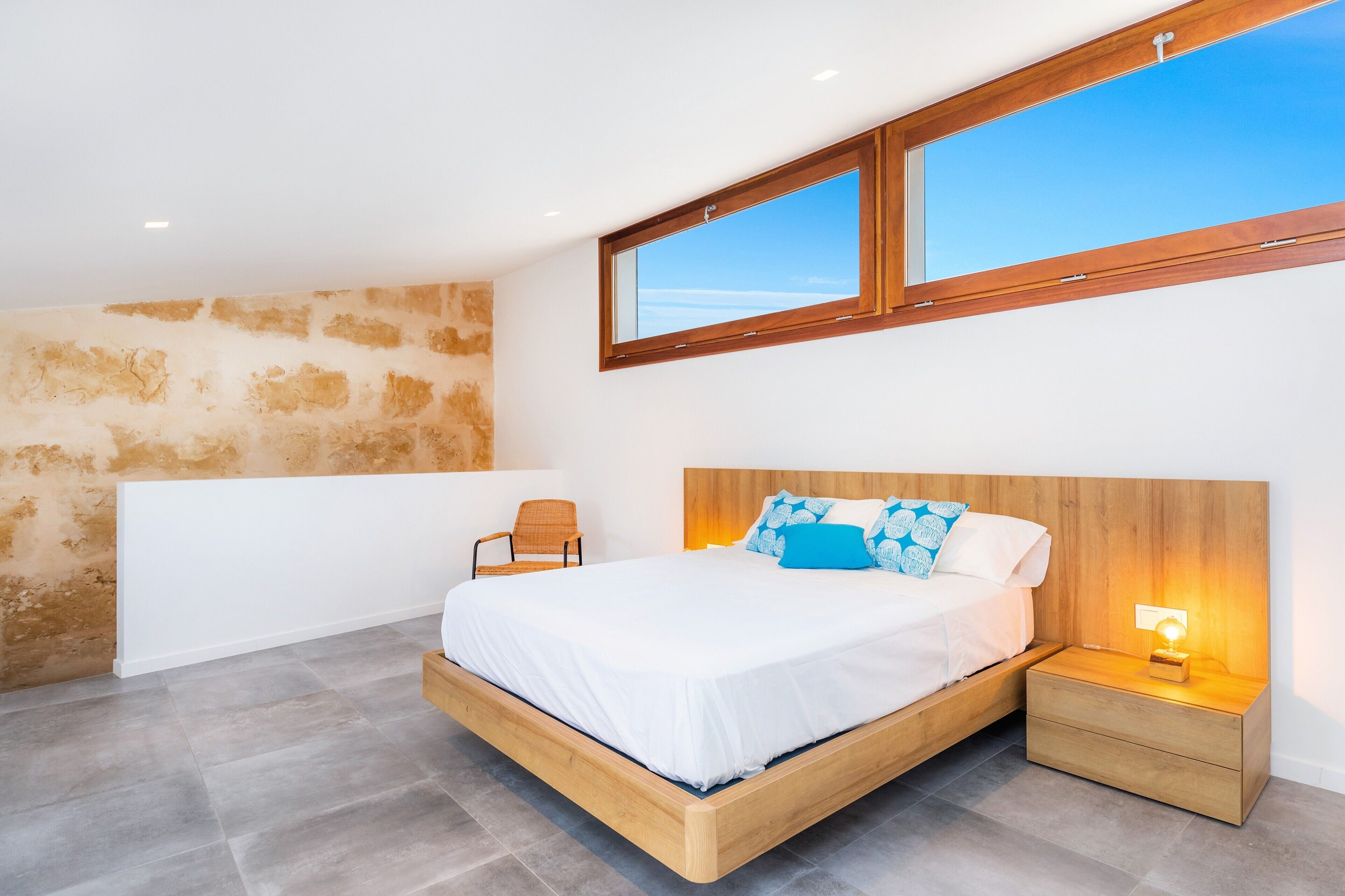 Een slaapkamer met een houten bed, een nachtkastje, een stoel en een groot raam.