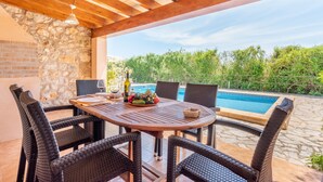 An outdoor patio with a round table, wicker chairs, a pool, and a stone wall. - Mediterranean Finca "Es Puch" with Mountain view, Balcony, Garden, Terrace & Pool (BUGER)
