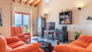 A living room with orange sofas, a glass coffee table, a television, a bookshelf, and a ceiling light fixture. - Mediterranean Finca "Es Puch" with Mountain view, Balcony, Garden, Terrace & Pool (BUGER)