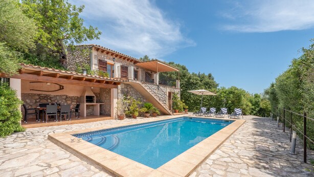 A stone pool with a stone deck, outdoor furniture, and a two-story house with a balcony. - Mediterranean Finca "Es Puch" with Mountain view, Balcony, Garden, Terrace & Pool (BUGER)