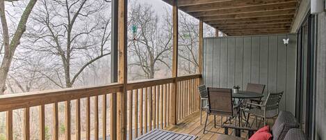 A covered outdoor deck with wooden furniture, including a table and chairs, and a sofa with cushions.
