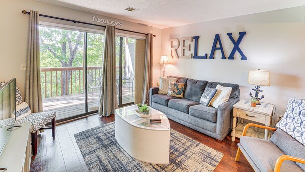 A living room with a grey sofa, a white coffee table, and a large 'RELAX' sign on the wall. - 2 Mi to Silver Dollar City: Reed Springs Condo (Reeds Spring)