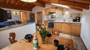 Een moderne keuken met houten kastjes, een eethoek met een houten tafel, en een blauwe bank in de woonkamer.