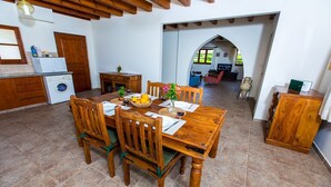 A dining area with a wooden table set for four, surrounded by chairs. A washing machine is visible in the background, and there is a small cabinet to the right. - Charming Villa, Private Pool, Hot Tub, Sea Views close to the Pretty Fishing Harbour at Pomos! (Pomos)