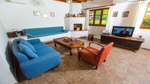 A living room with a blue sofa, a red armchair, a wooden coffee table, and a television on a wooden stand. - Charming Villa, Private Pool, Hot Tub, Sea Views close to the Pretty Fishing Harbour at Pomos! (Pomos)