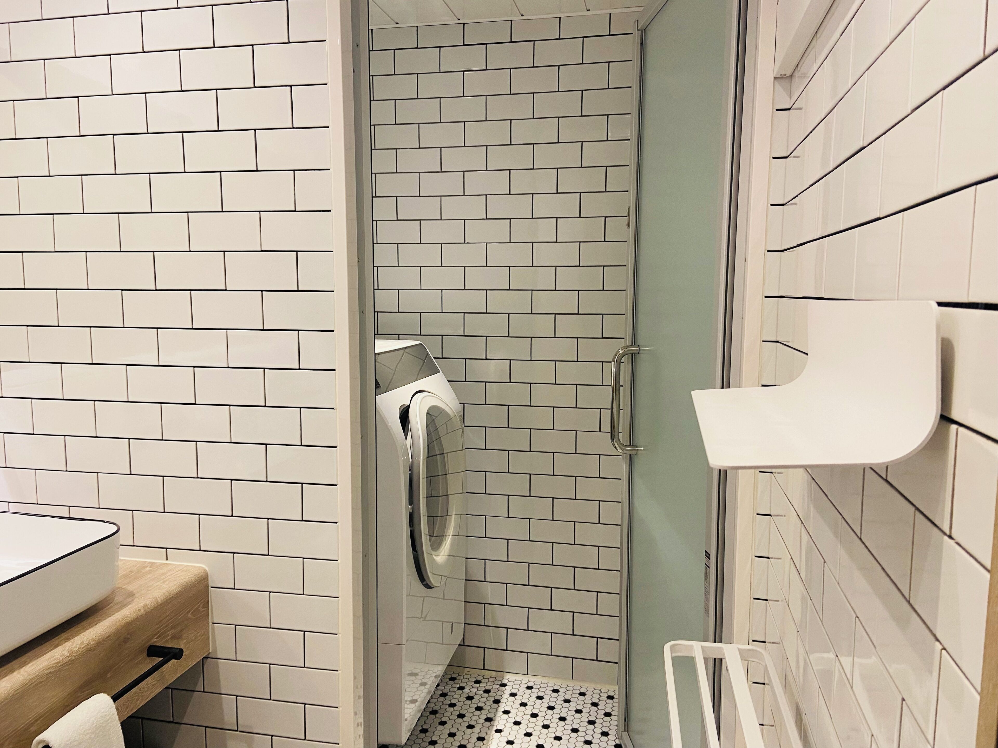 A bathroom with white subway tiles, a glass shower enclosure, a white sink, and a towel rack.