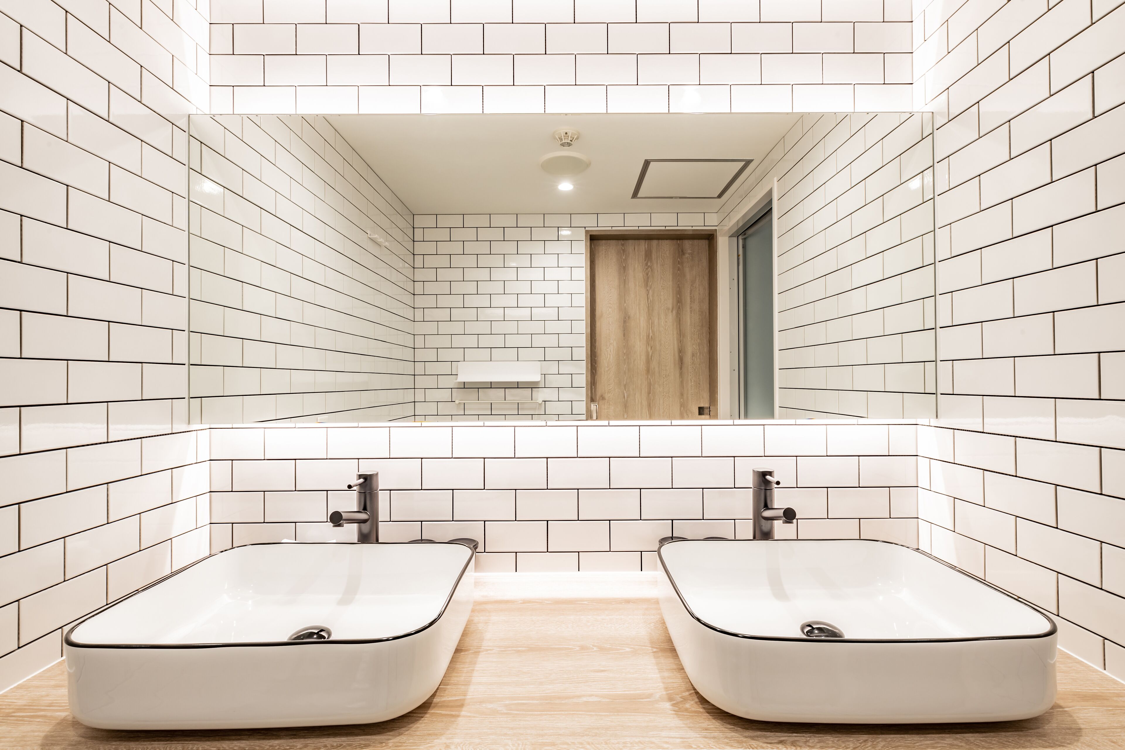 A modern bathroom with white subway tiles, a wooden door, and two sinks.