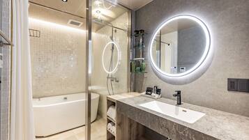 Un baño moderno con bañera, tocador con lavabo y un espejo grande con luz circular.