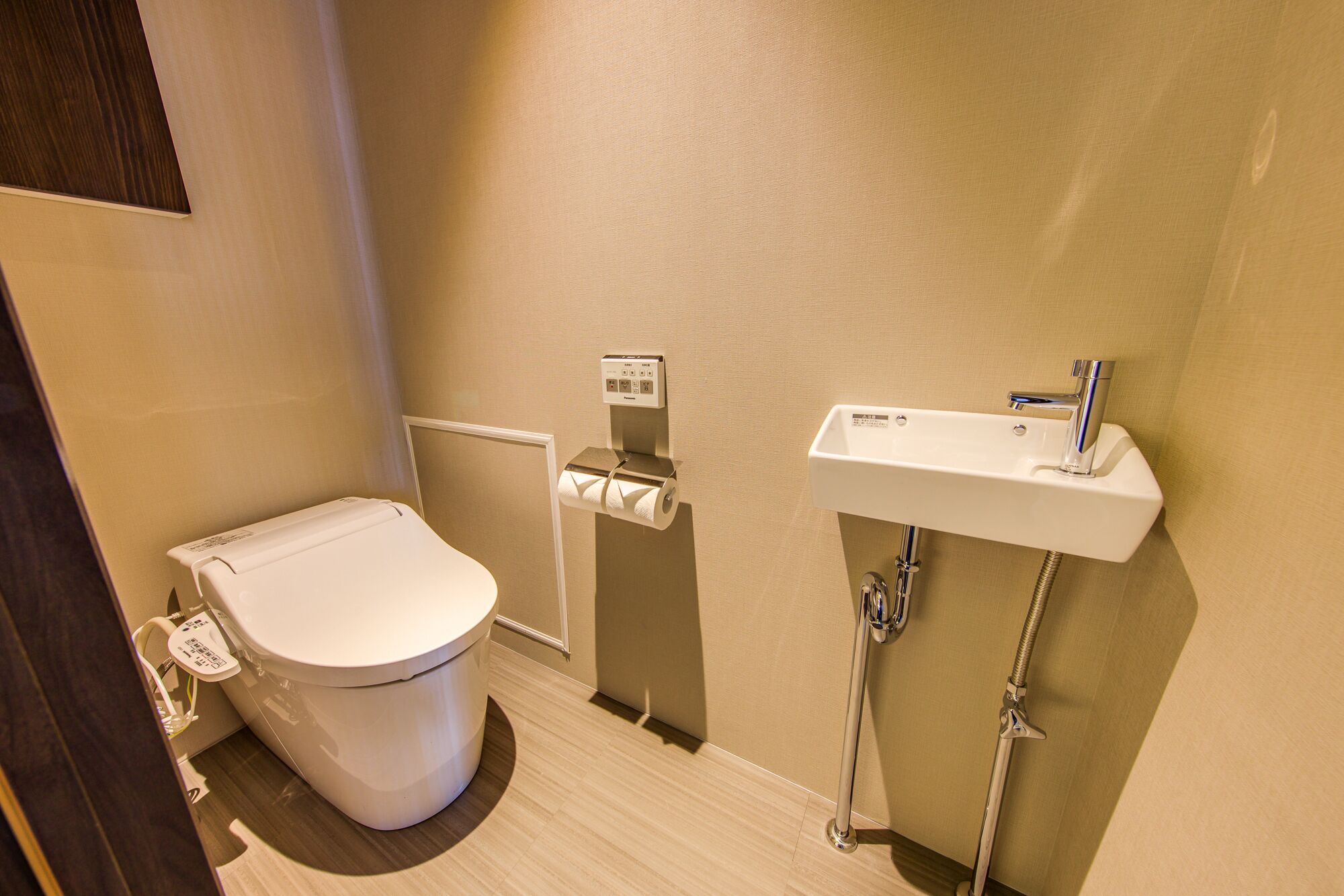 A compact bathroom with a toilet, a paper towel dispenser, and a sink with a faucet.