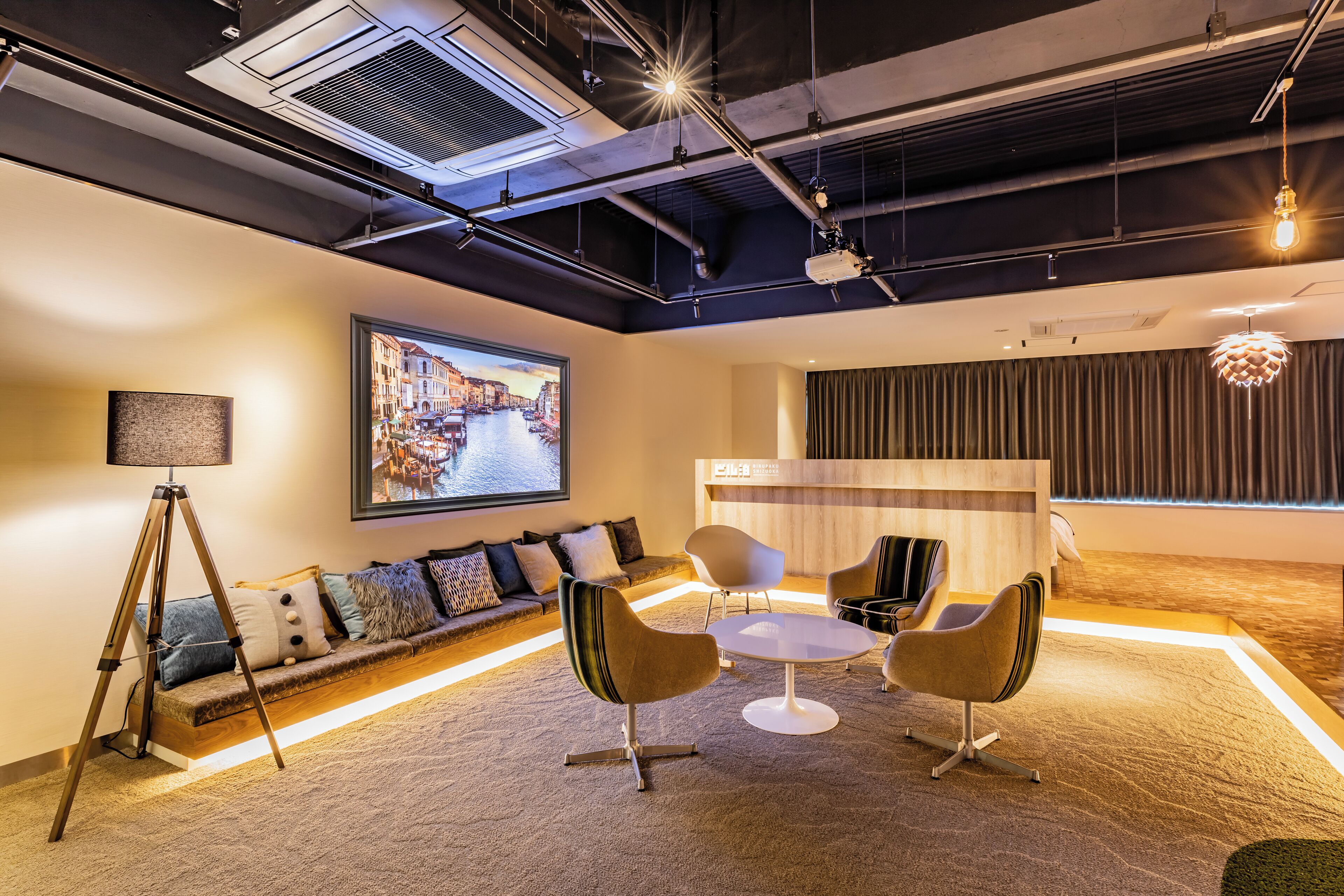 Une salle de conférence moderne dotée d’un grand écran, d’un comptoir d’accueil en bois et de sièges contemporains.